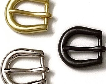 Könnte beinhalten: Drei Metall-Gürtelschnallen in verschiedenen Ausführungen: Gold, Schwarz und Silber. Jede Schnalle hat einen D-förmigen Rahmen mit einem Doppelzinkenverschluss.