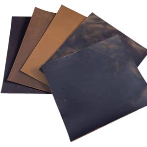 Puede incluir: Una colección de hojas de cuero en varios tonos de marrón y negro. Las hojas están dispuestas en forma de abanico, mostrando los diferentes colores y texturas del material. Los colores varían del azul marino oscuro al marrón claro.