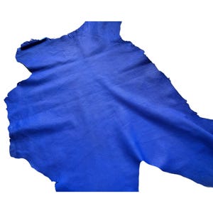 May include: A piece of blue leather with a textured surface. The leather has a natural shape with irregular edges and a slightly wrinkled appearance. The color is a vibrant, saturated blue.