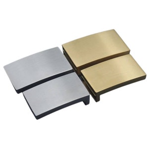 May include: Two metal watch band buckle clasps, one silver and one gold. The clasps are curved and have a brushed finish.