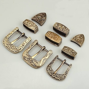May include: A set of eight ornate brass belt buckles, featuring intricate floral and dragon designs. The buckles are in various shapes and sizes, including rectangular, square, and oval.