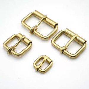 May include: Four brass belt buckles of different sizes. The buckles are all gold in color and have a smooth, polished finish.