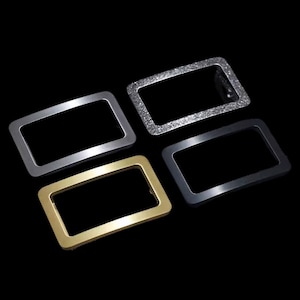 May include: Four metal belt buckles in different finishes: silver, gold, black, and a textured silver. The buckles are rectangular with rounded corners and a smooth, polished surface.