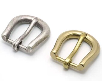 Könnte beinhalten: Zwei Metall-Gürtelschnallen, eine silberne und eine goldene. Beide Schnallen haben die Form eines Hufeisens mit abgerundetem Oberteil und flachem Boden.