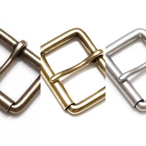May include: Three metal belt buckles in different finishes: silver, brass, and antique brass. Each buckle is a simple, rectangular design with a smooth, polished finish.