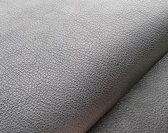 Op de afbeelding: Een close-up van een zwart materiaal met een uitgesproken korrelige textuur. Het oppervlak vertoont een consistent korrelpatroon met kleine, verhoogde bultjes over het hele gebied, wat een matte afwerking creëert met subtiele highlights langs de vouw.