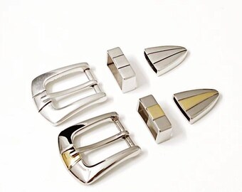 May include: A set of five silver belt buckles, two of which have a gold accent. The buckles are all different shapes and sizes.