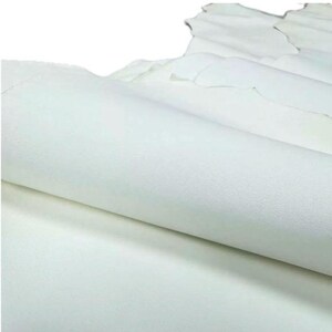 May include: A close-up of a stack of white leather hides. The leather is smooth and appears to be soft. The edges of the leather are slightly uneven, suggesting a natural cut. The hides are layered, with some rolled up.