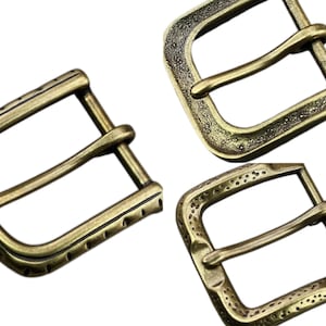 Puede incluir: Tres hebillas de cinturón de latón antiguo con diferentes diseños texturizados. Las hebillas tienen forma rectangular con una sola barra y un pasador para asegurar un cinturón. El latón tiene un aspecto cálido y envejecido.