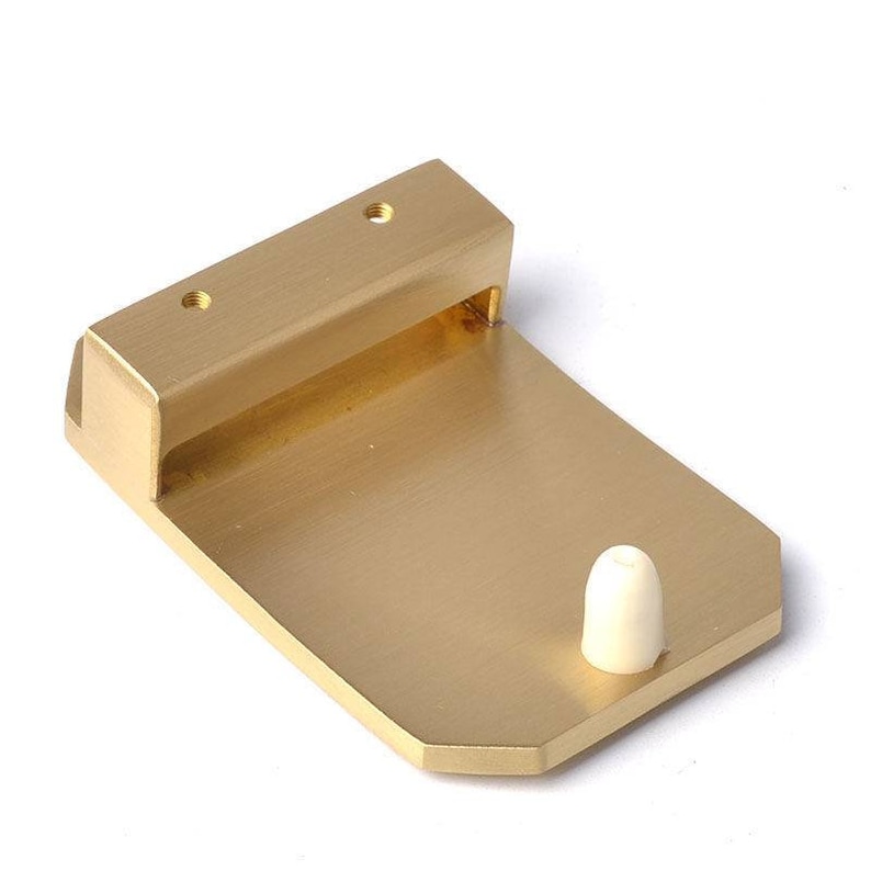 K&ouml;nnte beinhalten: Ein goldfarbener T&uuml;rstopper aus Metall mit einem wei&szlig;en Kunststoffstopfen. Der T&uuml;rstopper hat eine rechteckige Basis und einen erh&ouml;hten Abschnitt mit zwei Schraubenl&ouml;chern.