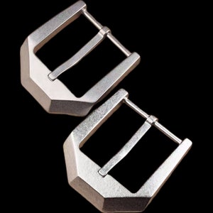 May include: Two silver metal belt buckles with a brushed finish. The buckles have a rectangular shape with a rounded edge and a single prong.