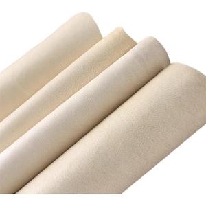 May include: Close-up of a stack of off-white leather sheets. The leather has a textured surface and a slightly grainy appearance.