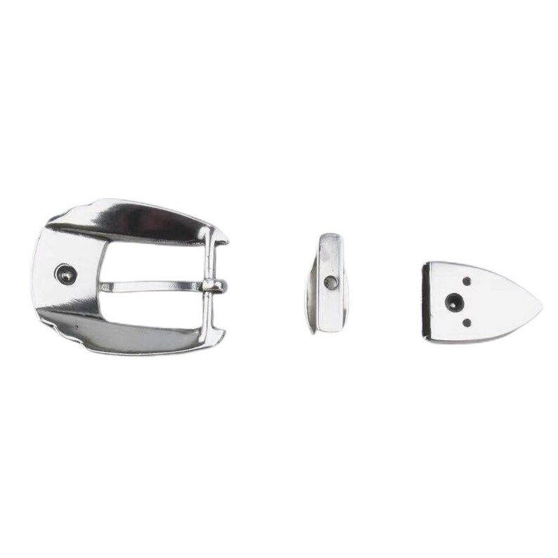 Puede incluir: Una hebilla de cintur&oacute;n de metal plateado con un dise&ntilde;o liso y curvo. La hebilla tiene una sola punta y un peque&ntilde;o agujero redondo en la parte superior. La hebilla se muestra con dos piezas de metal separadas, una rectangular y otra con forma de peque&ntilde;o tri&aacute;ngulo puntiagudo.