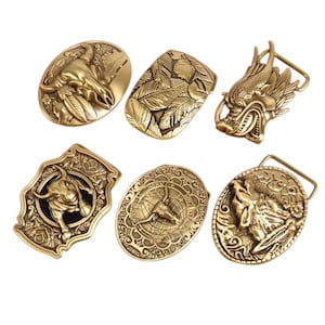 Puede incluir: Seis hebillas de cinturón doradas con diferentes diseños. Las hebillas presentan un toro, un dragón, un lobo, plumas y un toro con un globo terráqueo.