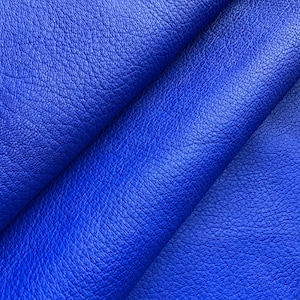 Puede incluir: Primer plano de tela de cuero azul vibrante. El material tiene una superficie texturizada con sutiles variaciones de color y tono. Los pliegues y arrugas añaden profundidad y dimensión al textil.