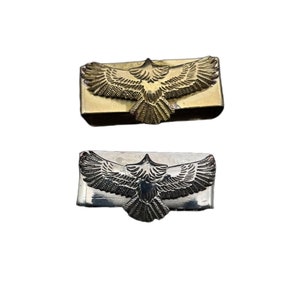 May include: Two metal belt buckles featuring an eagle design. The top buckle is gold and the bottom buckle is silver.