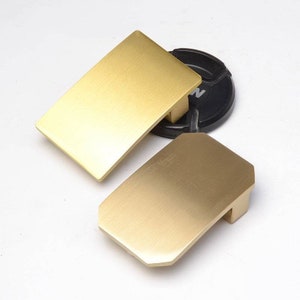 Può includere: Due fibbie per cintura in metallo color oro. Una fibbia è rettangolare e l'altra è un rettangolo leggermente arrotondato.