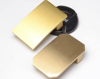 May include: Two gold-colored metal belt buckles. One buckle is rectangular and the other is a slightly rounded rectangle.