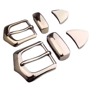 May include: A collection of shiny, silver-toned metal belt buckles and matching accessories. The set includes two rectangular buckles with a classic design, two rectangular pieces, and two triangular pieces, all with a polished finish.