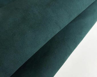 May include: Close-up of a folded piece of dark teal fabric. The material has a soft, velvety texture and a subtle sheen. The folds create shadows and highlights, enhancing the depth and texture of the fabric.