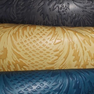 Puede incluir: Primer plano de tres rollos texturizados en tonos azul, beige y gris oscuro. Los rollos tienen un patrón repetitivo de formas orgánicas en relieve, creando una superficie táctil. Los colores y texturas sugieren un enfoque en materiales de diseño o artesanía.