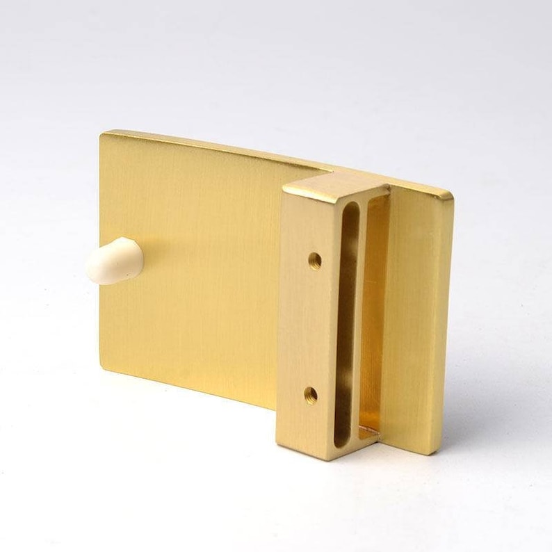 K&ouml;nnte beinhalten: Eine goldfarbene G&uuml;rtelschnalle aus Metall mit glatter, geb&uuml;rsteter Oberfl&auml;che. Die Schnalle hat eine rechteckige Form mit einem Schlitz f&uuml;r einen G&uuml;rtelriemen und zwei kleinen L&ouml;chern an der Seite.