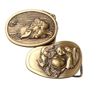 Puede incluir: Dos hebillas de cinturón de metal dorado con diseños ornamentados. Una hebilla presenta una figura sentada en una nube con un bastón y un mono. La otra hebilla presenta una figura con una gran barriga y una cara sonriente.
