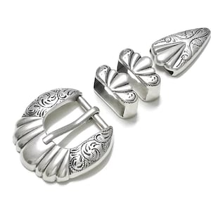 May include: Silver belt buckle set with an ornate design. The set includes a buckle, two belt loops, and a tip.