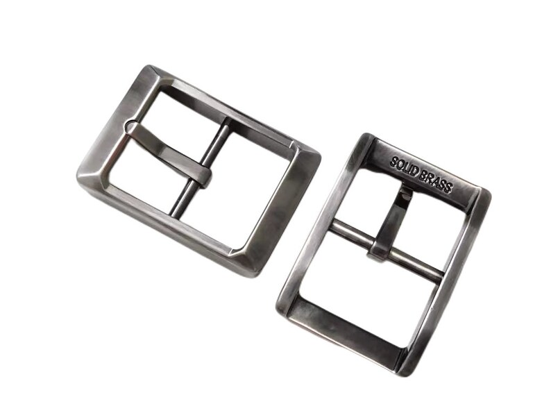 Pu&ograve; includere: Due fibbie per cintura in metallo argentato. La fibbia a destra ha le parole "SOLID BRASS" incise.
