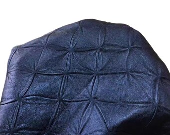 May include: Close-up of a section of dark blue leather with a quilted pattern. The leather has a textured surface and is stitched in a geometric design, creating a series of diamond shapes.