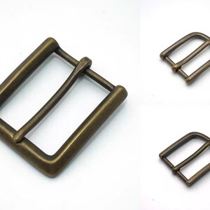 May include: Two antique brass belt buckles. The larger buckle is rectangular with a smooth finish. The smaller buckle is a simple D-ring shape.