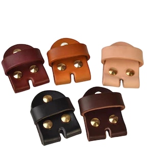 Peut inclure: Cinq boucles de ceinture en cuir de différentes couleurs : marron, beige, rose clair, noir et marron foncé. Chaque boucle est dotée de deux rivets en laiton et d’une fente pour une ceinture.