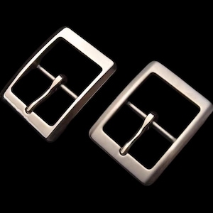 Peut inclure: Deux boucles de ceinture en métal argenté. Les boucles sont rectangulaires avec une finition lisse et polie.