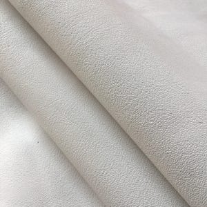 May include: Close-up of a folded piece of off-white textured fabric. The material has a subtle, pebbled surface, with soft folds and shadows. The fabric appears to be a light, neutral color, suitable for various crafting projects.