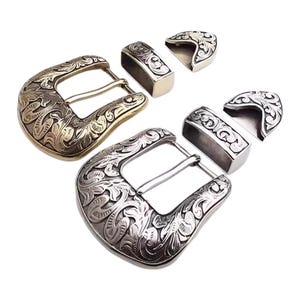 May include: Two ornate belt buckles with matching keepers and tips. One buckle is gold-toned, the other is silver-toned. All pieces feature a detailed floral scroll design, suitable for Western-style belts or accessories.