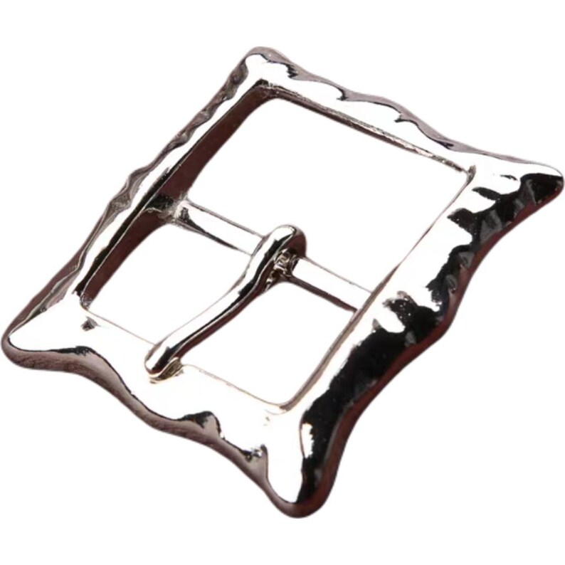 Op de afbeelding: Zilverkleurige metalen gesp met een getextureerde, onregelmatige vorm. De gesp heeft een rechthoekig frame met een gladde, afgeronde rand.