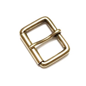 May include: A gold metal buckle with a rectangular frame and a single prong. The buckle is designed for use with leather straps.