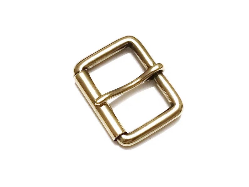May include: A gold metal buckle with a rectangular frame and a single prong. The buckle is designed for use with leather straps.