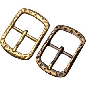 Peut inclure: Deux boucles de ceinture en métal avec une finition texturée. Une boucle est dorée et l'autre est de couleur laiton plus foncée.