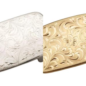 May include: Two belt buckles with an ornate floral design. One buckle is silver and the other is gold.