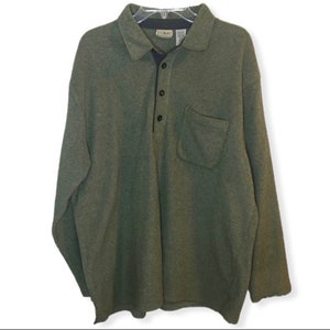 Puede incluir: Una camisa verde de manga larga con cuello, una solapa de botones y un bolsillo en el pecho izquierdo. La camisa tiene un sutil patrón jaspeado y el nombre de la marca "L.L.Bean" es visible en el cuello.