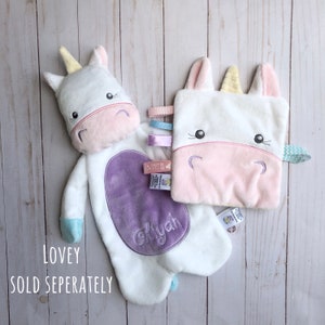 May include: Two white unicorn loveys with embroidered faces and pastel colored details. One lovey is a plush toy with a purple oval patch that says "Aaliyah". The other lovey is a smaller square with a pink face and a rainbow ribbon.