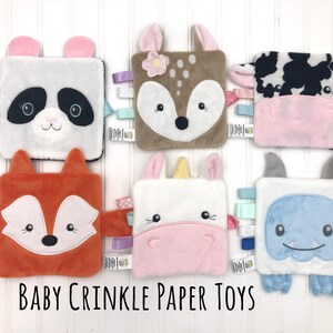 May include: Six plush baby crinkle paper toys with different animal faces. The toys are white with various colored accents and feature a panda, deer, cow, fox, unicorn, and monster.