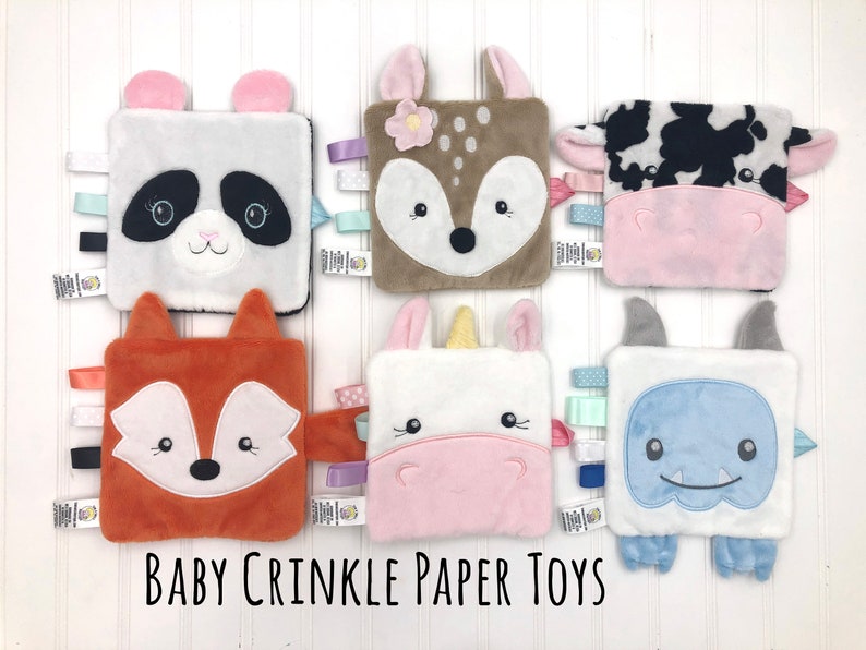 May include: Six plush baby crinkle paper toys with different animal faces. The toys are white with various colored accents and feature a panda, deer, cow, fox, unicorn, and monster.