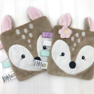 May include: Two brown plush fawn baby security blankets with pink ears and embroidered faces. One blanket has a pink flower and the other has a light blue, white, and purple ribbon.