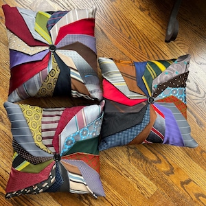 May include: Three decorative throw pillows made from repurposed neckties. Each pillow is a different color and features a unique pattern of ties arranged in a pinwheel design.