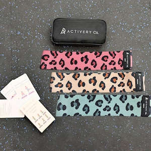 May include: Three leopard print resistance bands in pink, beige, and teal, with a black case and exercise cards. The bands are labelled "Light", "Medium", and "Heavy". The case is black with the text "ACTIVERY Co."