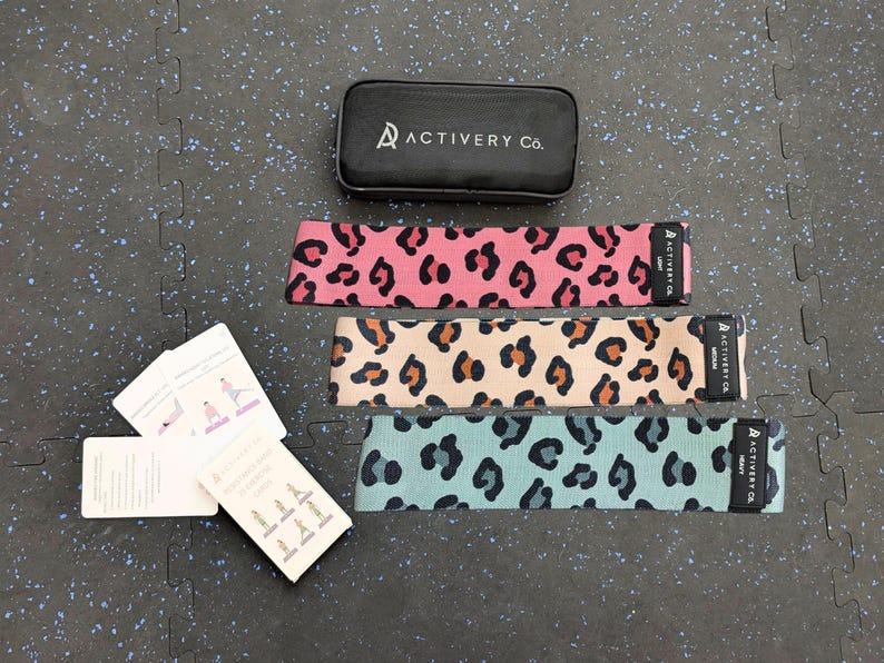 May include: Three leopard print resistance bands in pink, beige, and teal, with a black case and exercise cards. The bands are labelled "Light", "Medium", and "Heavy". The case is black with the text "ACTIVERY Co."