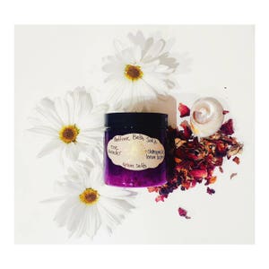 Peut inclure: Un pot violet de bain moussant avec une étiquette blanche qui indique "Bedtime Bath Soak" avec les ingrédients "rose lavande" et "camomille citron baumier" et le texte "Sels d'Epsom". Le pot est entouré de marguerites blanches et de pétales de roses séchés.