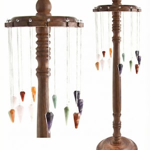 Könnte beinhalten: Zwei Holzständer mit mehreren Edelstein-Pendeln, die an Silberketten hängen. Die Pendel sind in verschiedenen Farben, darunter Orange, Grün, Lila und Weiß. Die Ständer sind aus dunklem Holz gefertigt.